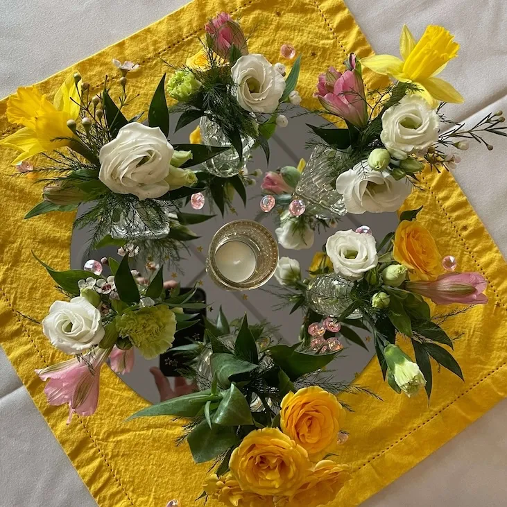 dainty baby shower centerpiece made with tiny bud vases holding flowers in a ring over a circular mirror and a yellow napkin.